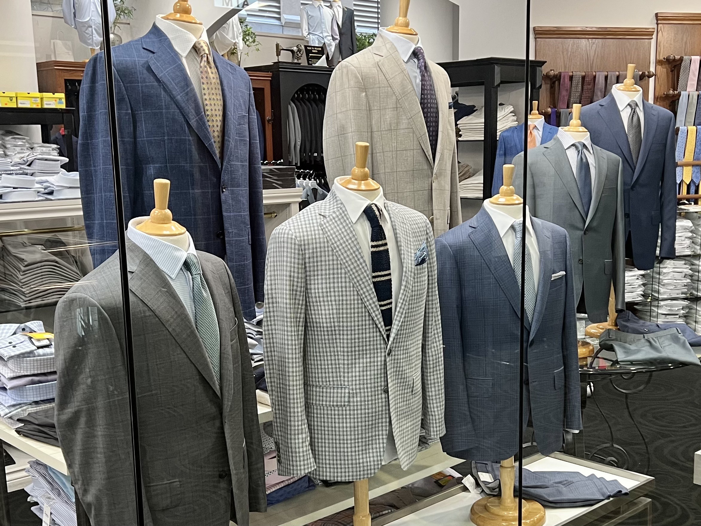 Tailored suits displayed on mannequins in a clothing store, showcasing a variety of styles and patterns